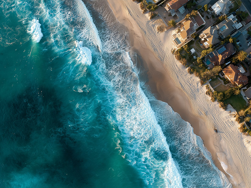 Aerial view of a sandy beach lined with colorful houses and lush greenery along the coastline