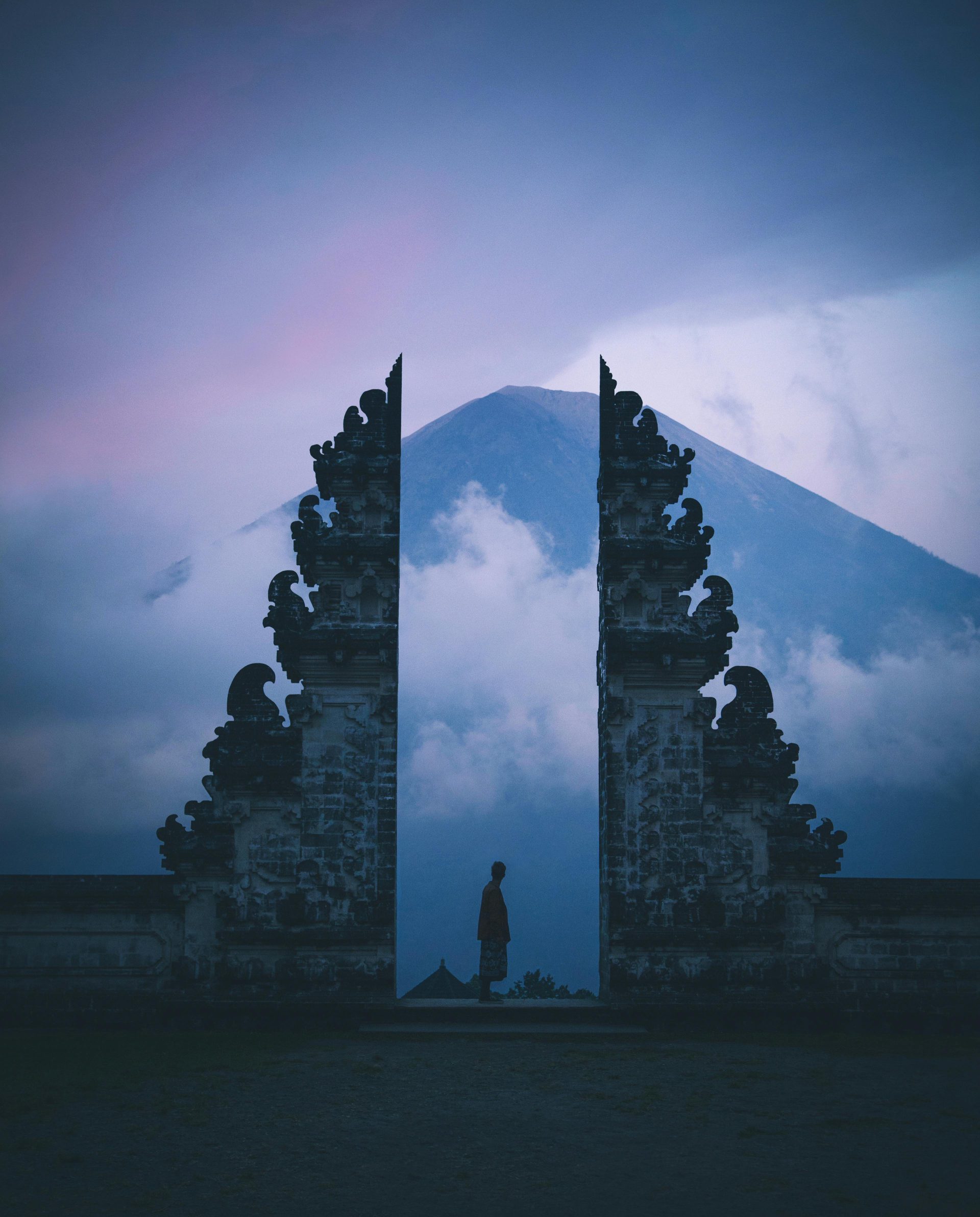 A person stands before a gate, with a majestic mountain rising in the background