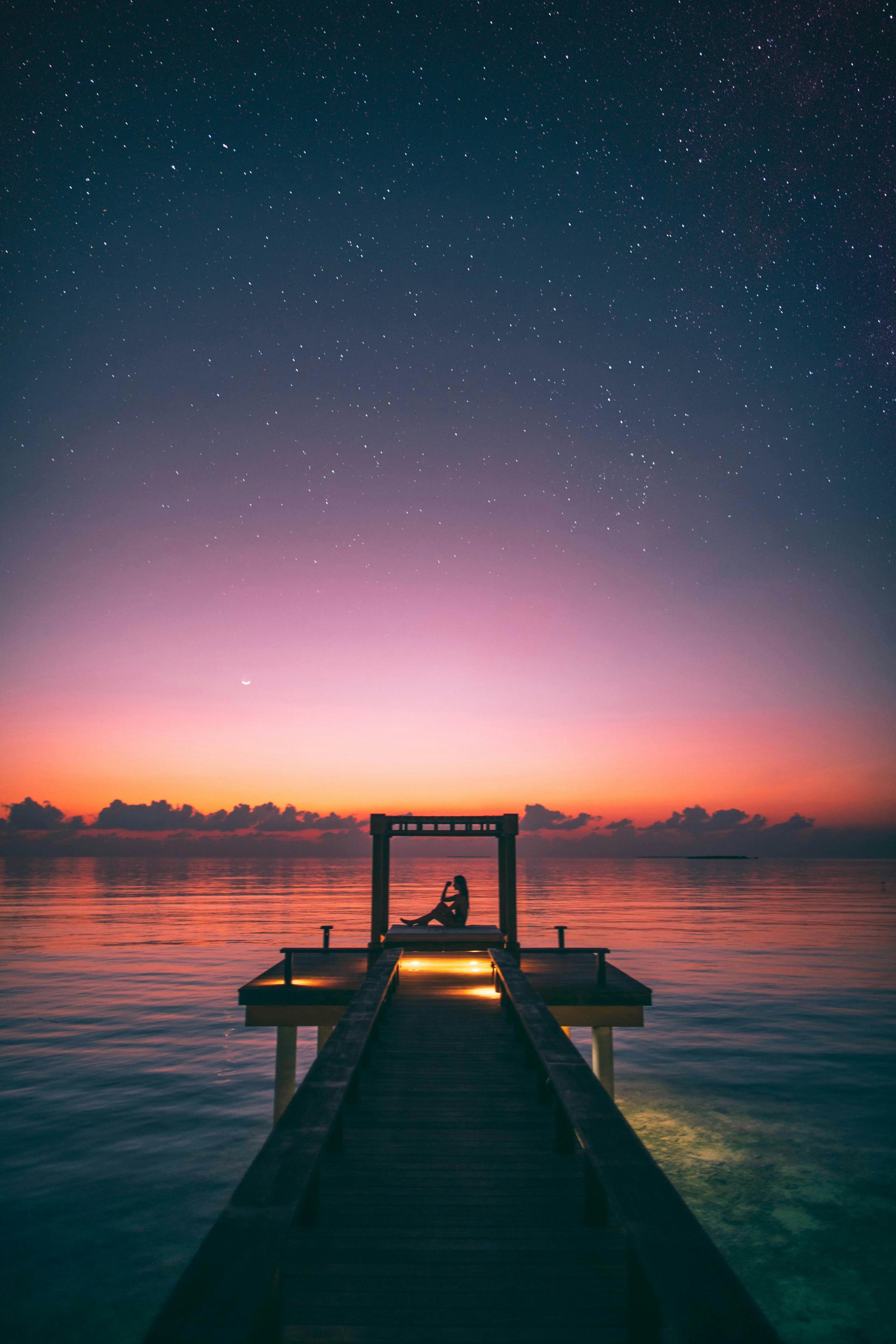 A weman relaxes on a dock, surrounded by the warm hues of a sunset over the water