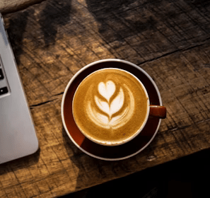 caffe latte on white ceramic cup beside silver and black laptop computer