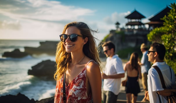 A woman in sunglasses and a floral dress stands on a beach with people in the background. A woman in sunglasses and a floral dress stands on a beach with people in the background.