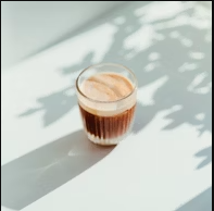 clear drinking glass with coffee on top of white table