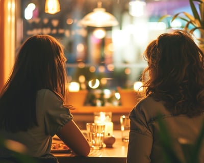 two women sitting at a table with candles and good food