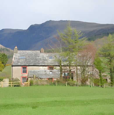 A house with a fenced in area with the mountains in the background in Holmrook, England