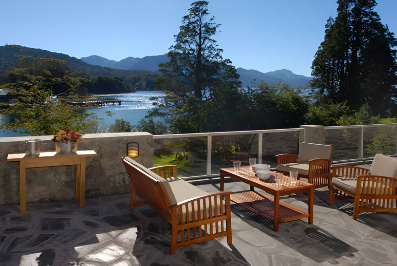 A patio with a table and chairs with the view of the mountains in llao llao, argentina A patio with a table and chairs with the view of the mountains in llao llao, argentina