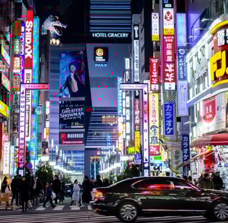 A bustling city street at night, filled with colorful neon signs and cars driving by