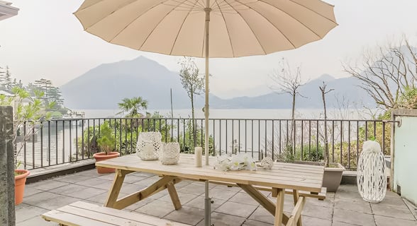 A balcony features a table and umbrella, providing a scenic view of the tranquil lake below.