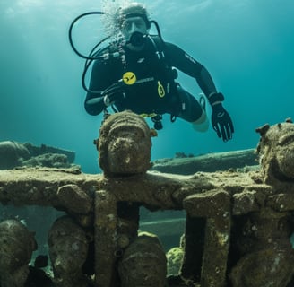 A scuba diver standing next to a large pile of statues underwater.