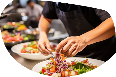 A chef tossing fresh vegetables in a bowl to prepare a salad in a restaurant kitchen A chef tossing fresh vegetables in a bowl to prepare a salad in a restaurant kitchen