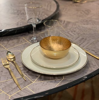 Table set with gold and white plates, along with a gold bowl. Table set with gold and white plates, along with a gold bowl.
