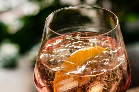 A glass of pink lemonade with ice cubes and a slice of lemon.