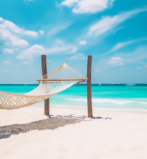 A serene beach scene with a hammock hanging between two palm trees, overlooking crystal clear turquoise waters under a bright blue sky.