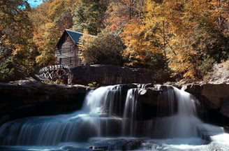 a waterfall in the woods with a cabin in the background