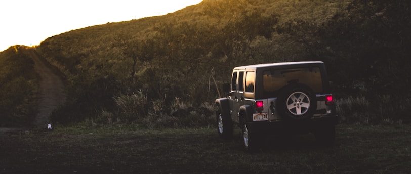 A jeep parked on a hillside at sunset, with the sky painted in warm hues of orange and pink.