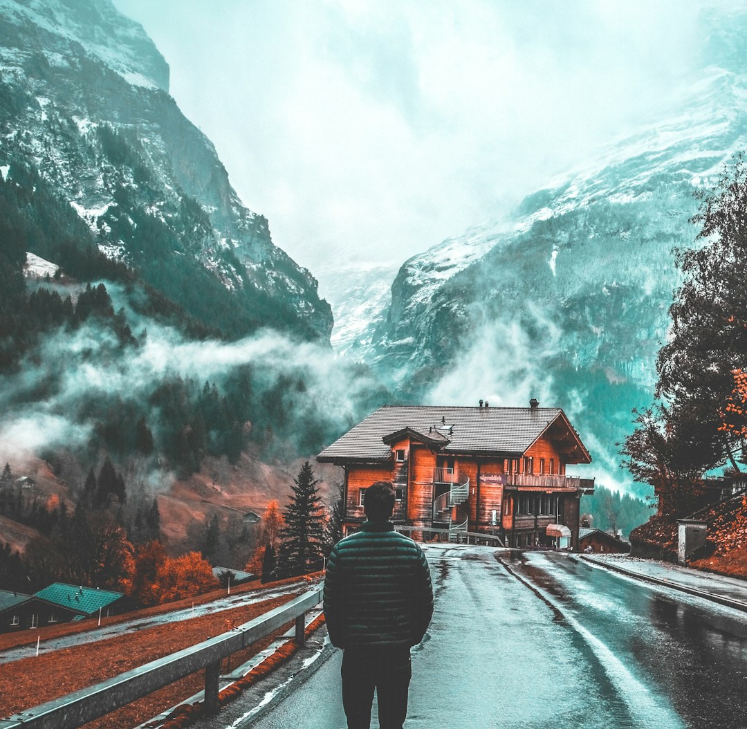 man standing on concrete pavement facing wooden house