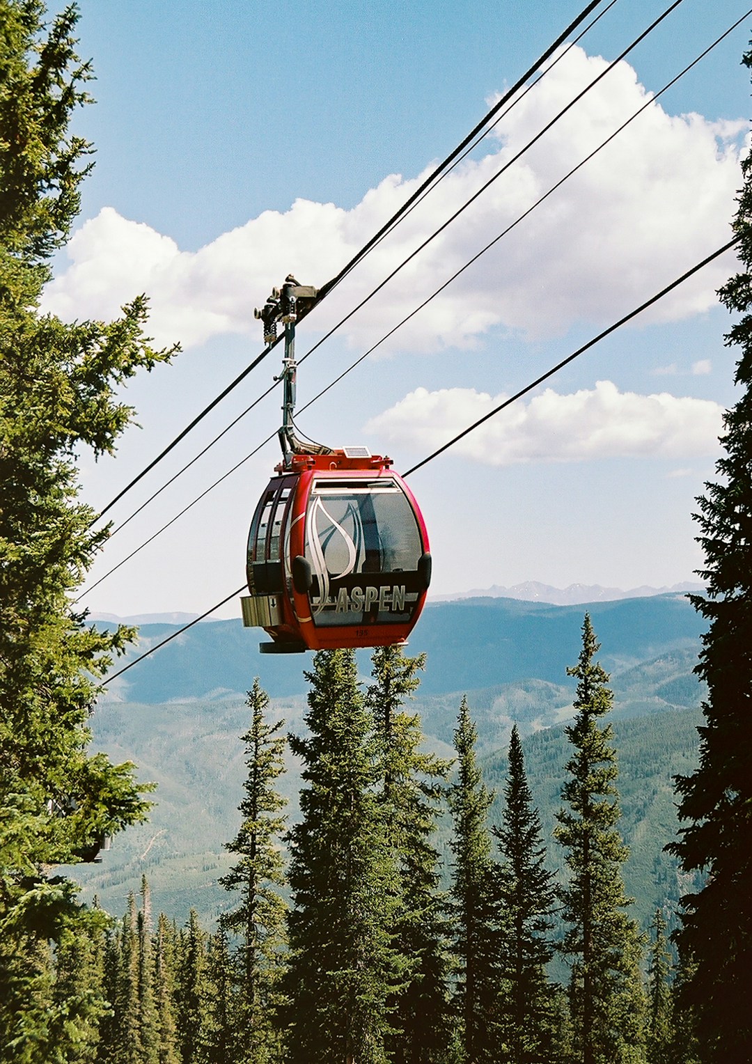 Red cable car over green trees during daytime