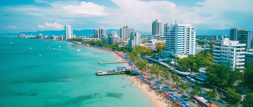 Aerial view of a coastline with tall buildings, a sandy beach, and people gathering near the shore with beach umbrellas and clear turquoise water