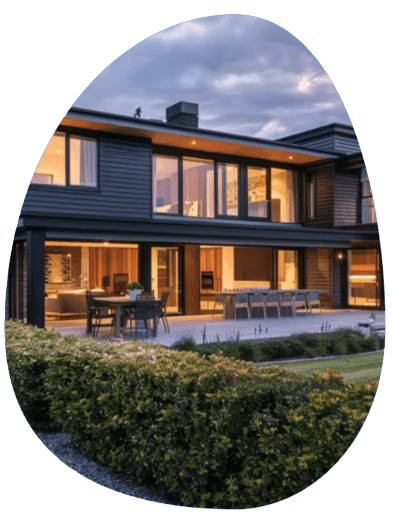 Modern black-clad holiday home in Kinloch, New Zealand, illuminated at twilight with a manicured hedge and wooden fence, near Modern black-clad holiday home in Kinloch, New Zealand, illuminated at twilight with a manicured hedge and wooden fence, near