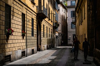 A man walking ahead on a narrow street, followed by a woman