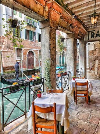 A picturesque restaurant featuring tables and chairs along a serene canal, inviting guests to enjoy the scenic view