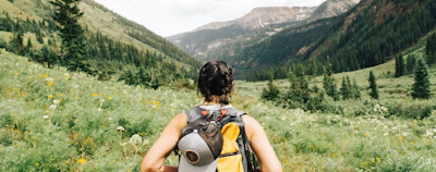person carrying yellow and black backpack walking between green plants