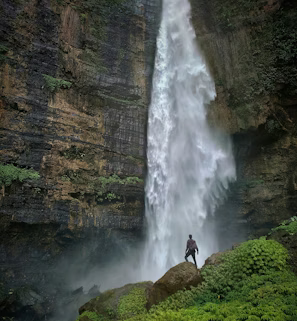 person standing on brown rock formation looking at waterfalls during daytime
