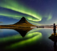 man standing beside the body of water with Aurora lights in the sky man standing beside the body of water with Aurora lights in the sky