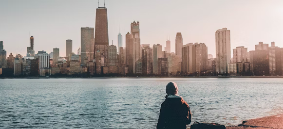 person sitting on path beside body of water with skyline buildings at distance person sitting on path beside body of water with skyline buildings at distance