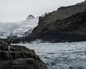 a man standing on top of a mountain next to a glacier a man standing on top of a mountain next to a glacier