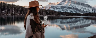 woman in brown coat wearing brown hat standing near lake during daytime woman in brown coat wearing brown hat standing near lake during daytime