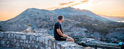 a man is sitting on a stone wall a man is sitting on a stone wall