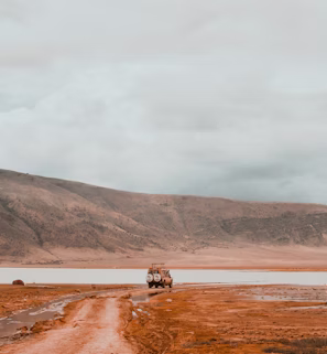 a truck driving down a dirt road next to a body of water a truck driving down a dirt road next to a body of water