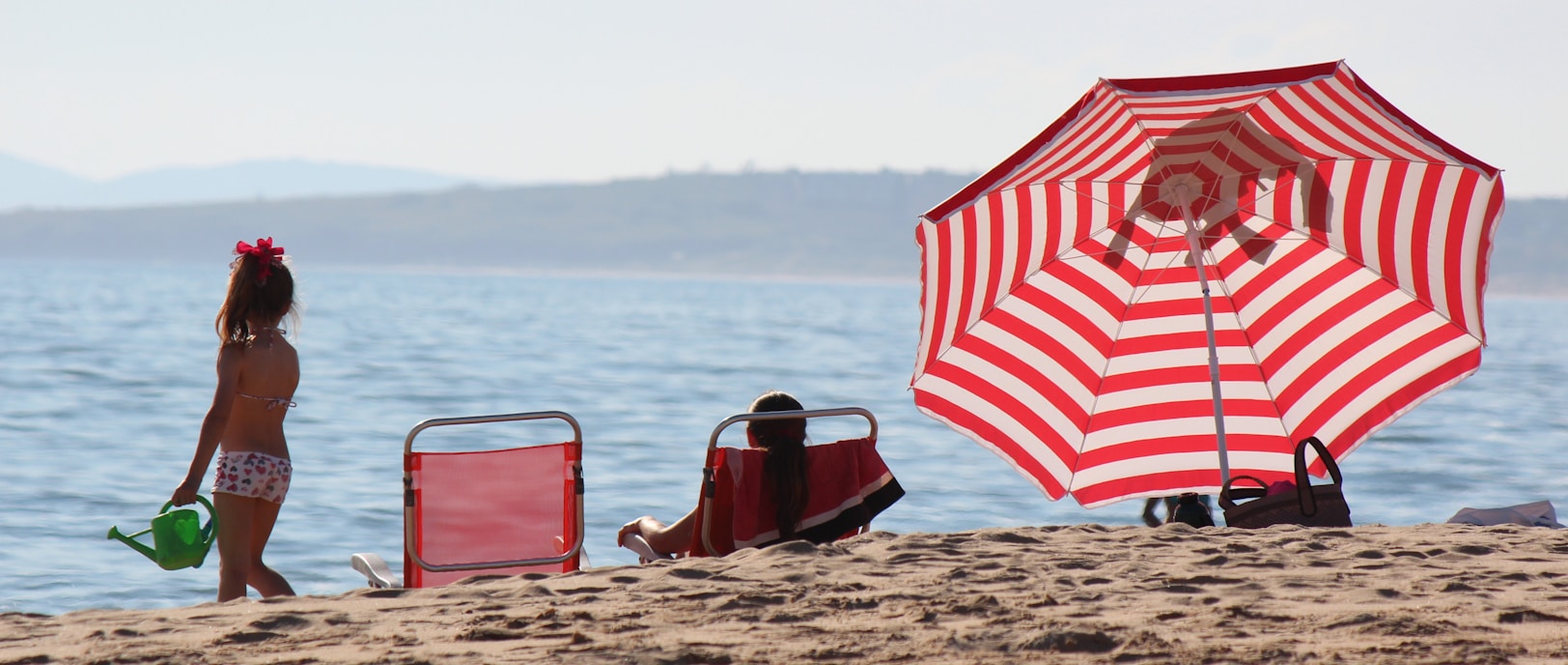 a little girl standing on a beach next to a red and white umbrella