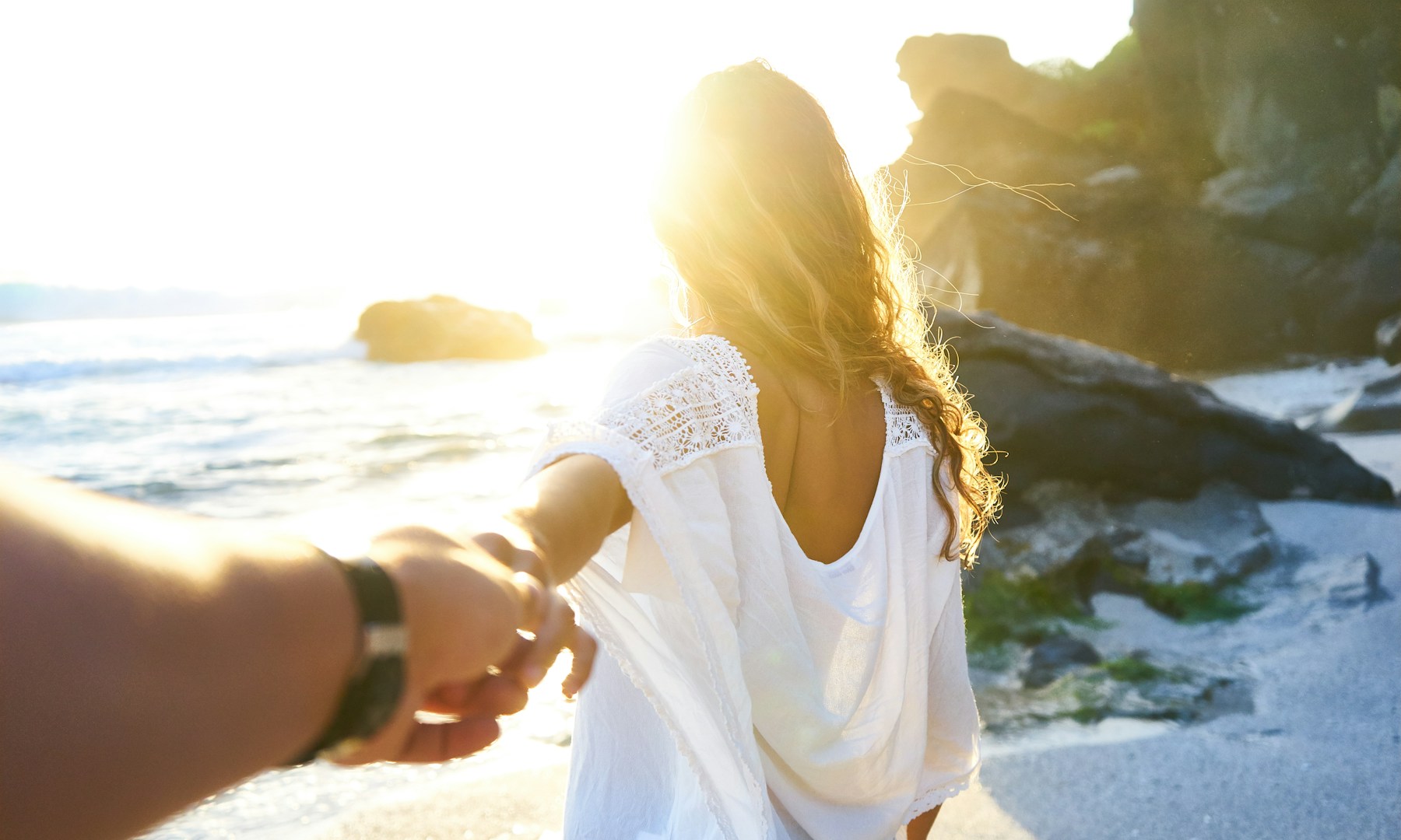 person holding woman's hand beside sea while facing sunlight