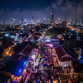 A drone shot of a rooftop party overlooking the city streets of Bangkok, Thailand at night.